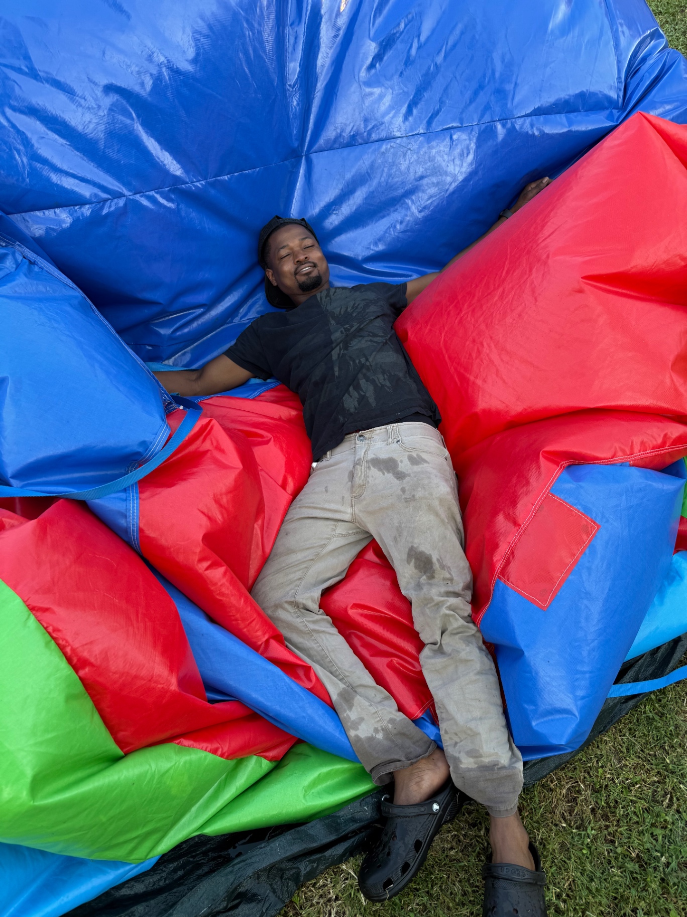 A Jump & Jam family member resting on folded inflatables in the grass after a day of setups