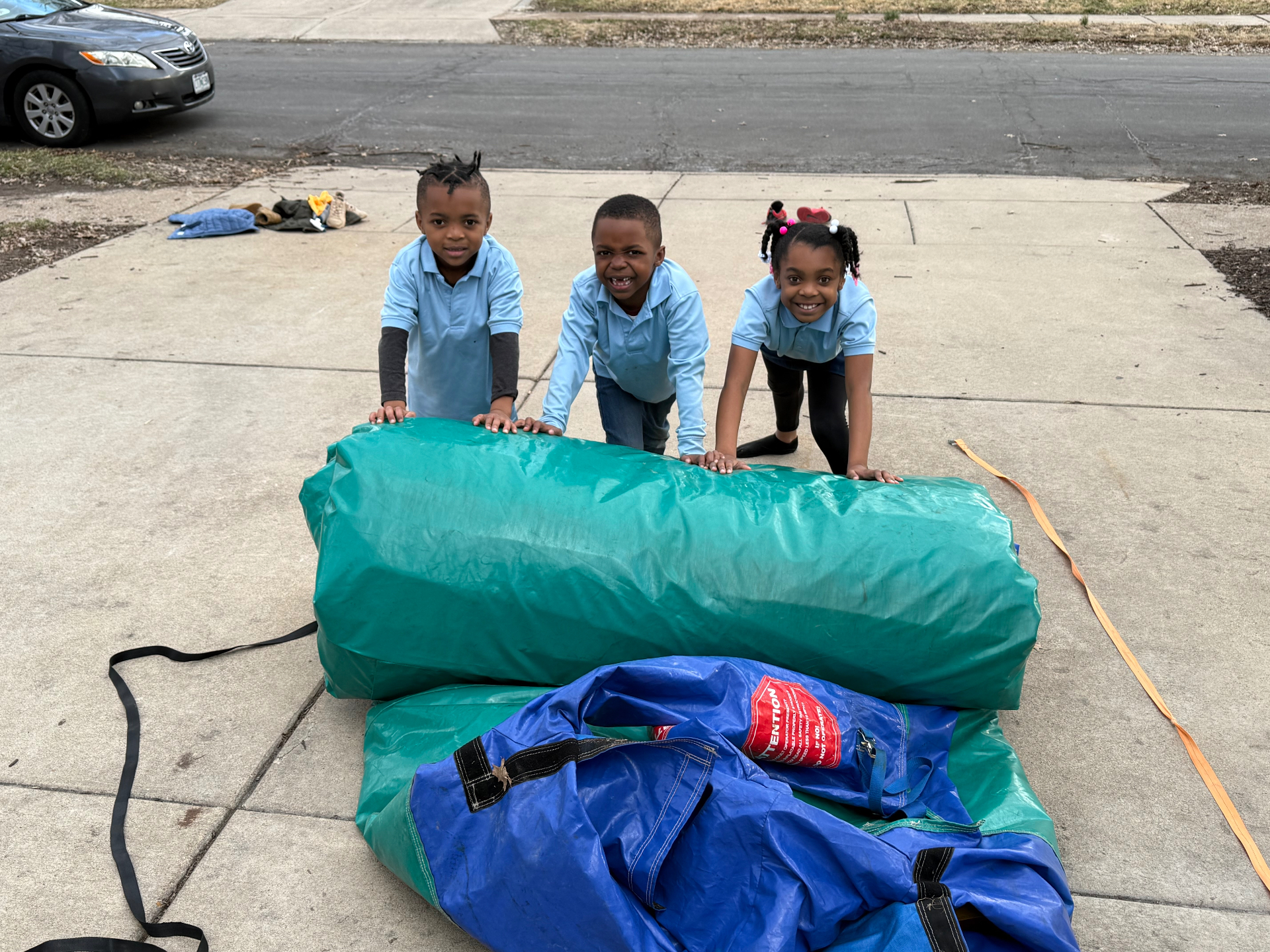 Three children helping push a rolled-up inflatable on the driveway before it is loaded
