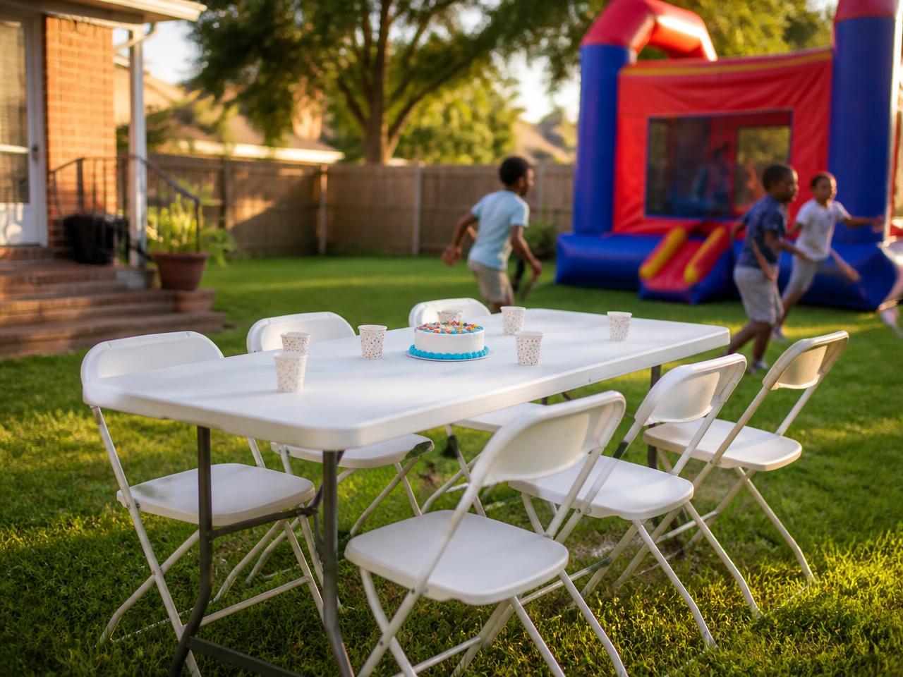 Example party setup: a 6-foot white folding table with six white folding chairs on a backyard lawn